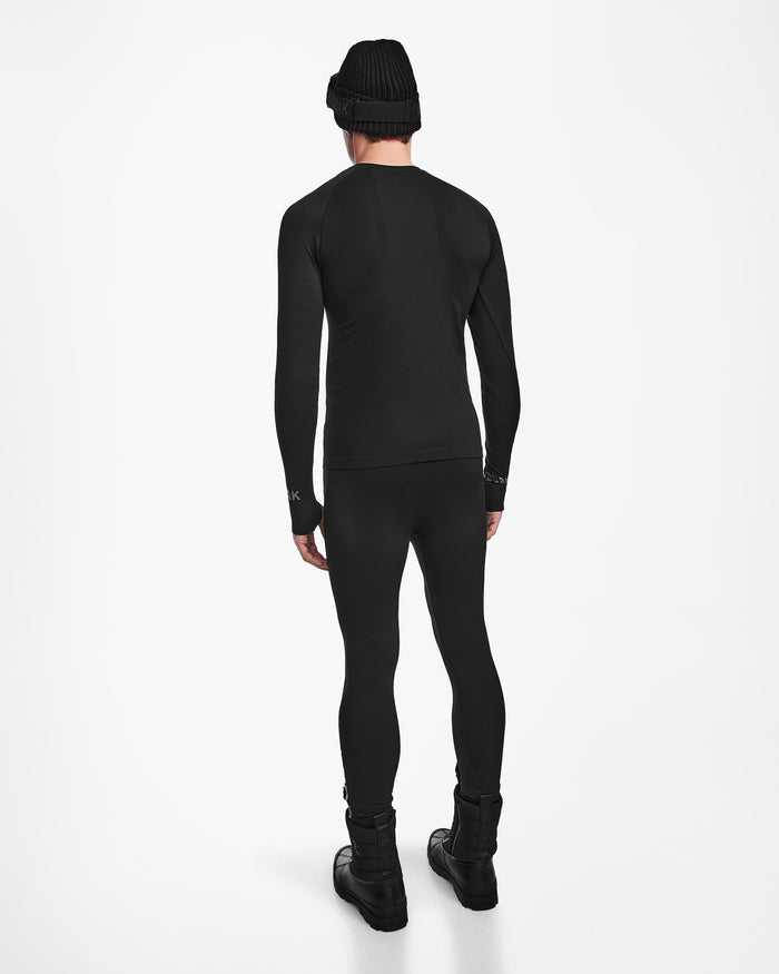 A person wearing the Rudsak FRANC - 6524541 Black beanie, black stretch long-sleeve top and leggings, and black boots stands facing away from the camera against a plain white background.