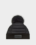 The GALA - 8424514 Black by Rudsak is a women’s quilted down puffer hat with a wide ribbed cuff, front rectangular logo patch, and a large removable faux fur pom pom, shown on a plain light background.