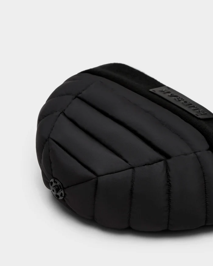 Close-up of the Rudsak GALA - 8424514 Black bag, featuring black quilted padding, a small round black emblem, and a rectangular text patch on a smooth light gray background—perfect for fans of premium down insulation.