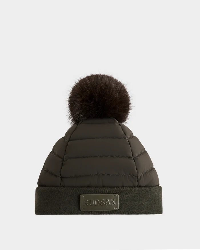 The Rudsak GALA - 8424514 Dark Olive is a women’s quilted down puffer hat with premium insulation, a large removable faux fur pom-pom, and a folded brim featuring a Rudsak logo patch. Shown on a plain white background.