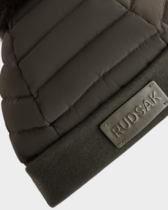 Close-up of the Rudsak GALA - 8424514 women’s down puffer hat in dark olive green, featuring a ribbed cuff with a rectangular embossed Rudsak patch, set against a plain white background.