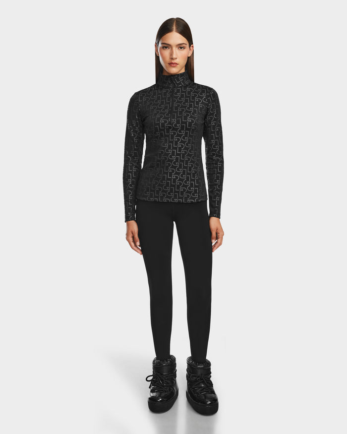 A woman with straight brown hair faces forward, wearing the Rudsak GASIA - 8524567 Black stretch active top and black leggings with chunky black boots against a plain white background.