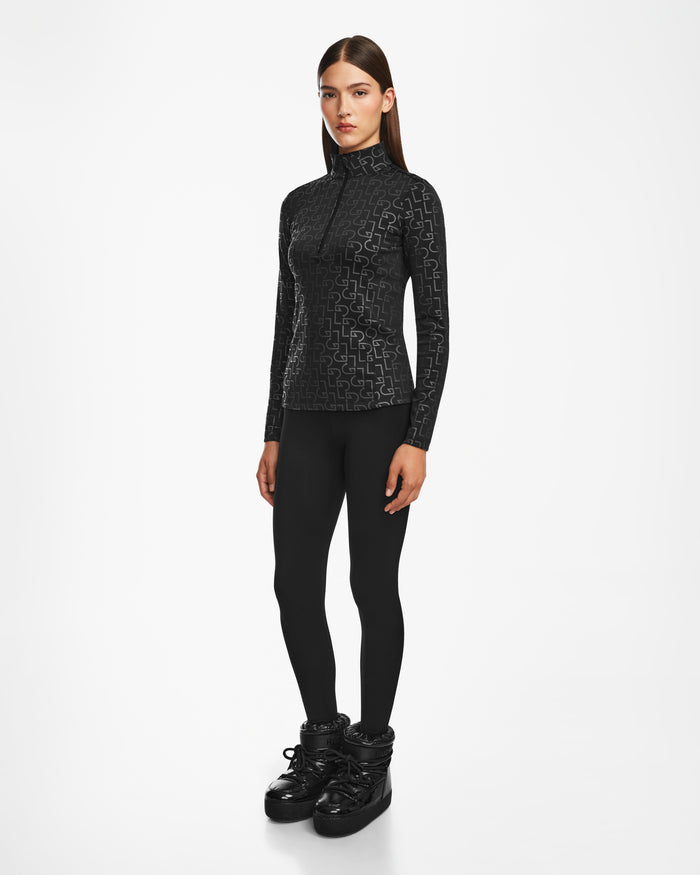 A woman with straight brown hair and a neutral expression models the GASIA - 8524567 Black stretch active top by Rudsak with black leggings and chunky boots, standing against a plain white background—ideal for cold-weather activewear.