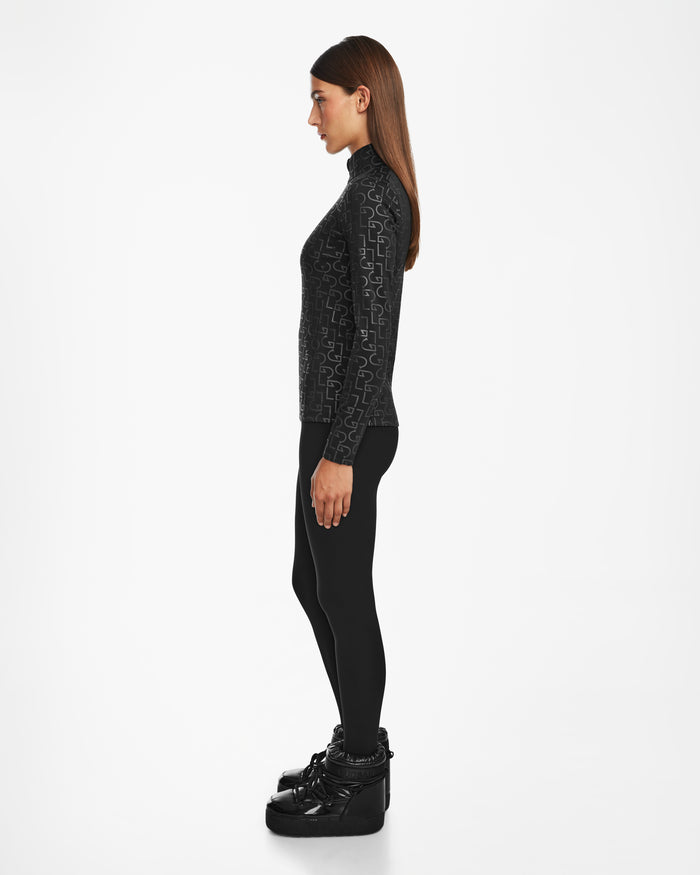 A woman with long, straight brown hair stands in profile against a white background, wearing the Rudsak GASIA - 8524567 Black zip-up mock neck top, black leggings, and glossy black winter boots.