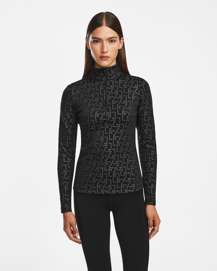 A woman with straight brown hair wears the Rudsak GASIA - 8524567 Black stretch active top, a fitted black mock neck zip-up with a geometric pattern, paired with black leggings against a white background—ideal cold-weather activewear.