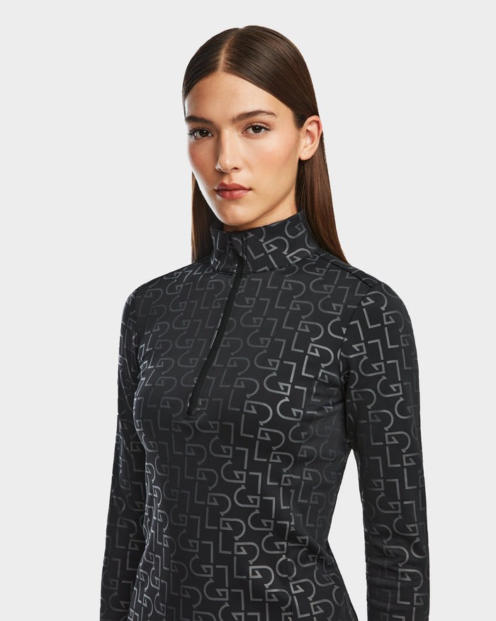 A woman with straight brown hair models the Rudsak GASIA - 8524567 Black women’s stretch active top, featuring a mock neck zip-up and geometric patterns, standing against a light gray background.
