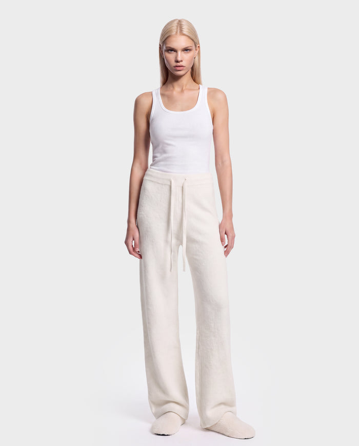 A person stands facing forward against a plain light background, wearing the Rudsak GENESIS - 8526506 Iceland cream-colored loose drawstring pants, paired with a white tank top and cream slippers.