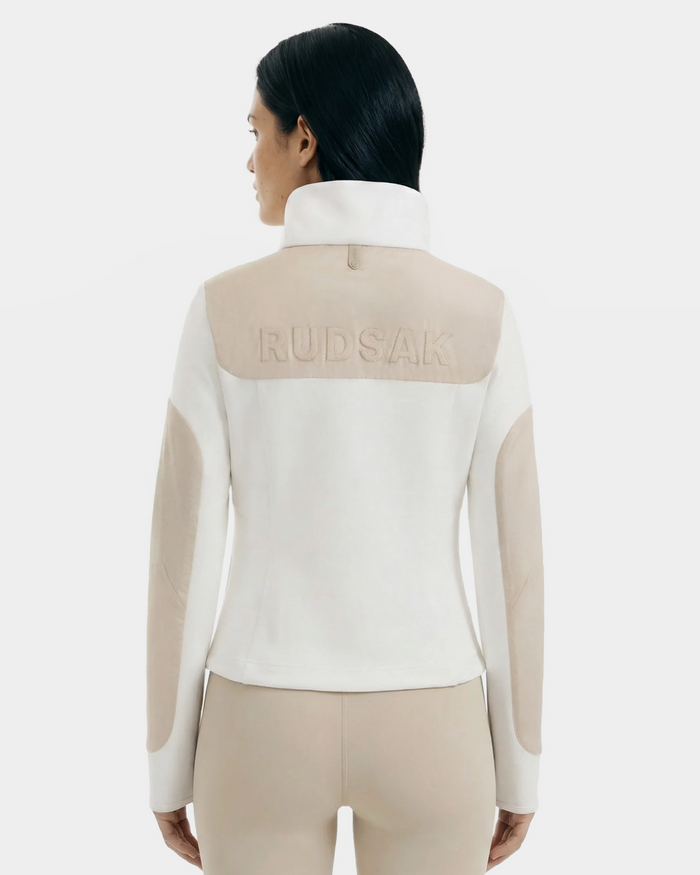 A woman with straight dark hair, seen from the back, wears the Rudsak GRANADA - 8126023 Vanilla sweater jacket with "RUDSAK" embossed on the upper back and matching beige pants against a plain light background.