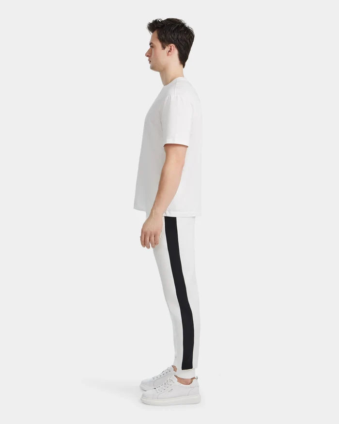 A man in profile, facing left, wears the Rudsak GRANT - 6525036 Iceland mens tee with a classic crewneck, paired with white athletic pants featuring a black side stripe and white sneakers, set against a plain white background.