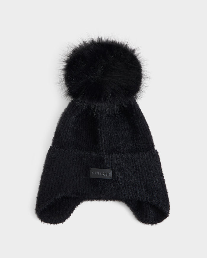 A black knit winter hat from Rudsak, the ICE - 8426519 Black model, featuring a large, fluffy pom-pom on top, ear flaps, and a small rectangular patch on the front. The hat is shown against a plain white background.