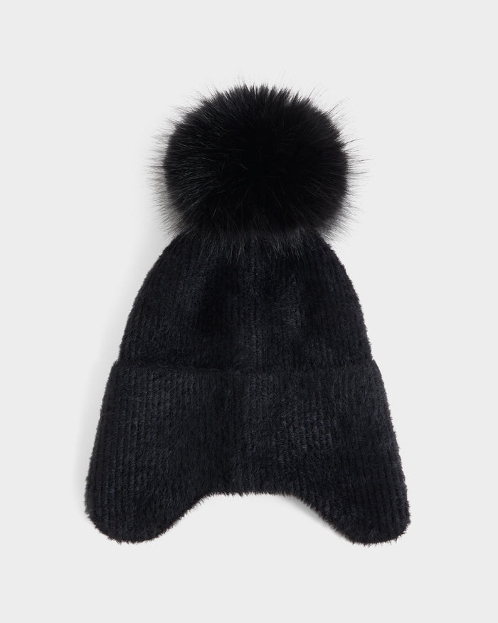 The Rudsak ICE - 8426519 Black is a black knitted beanie hat featuring ear flaps and a large, fluffy pom-pom on top, displayed against a plain white background.