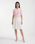 A woman poses against a white background, wearing the Rudsak IRIS - 8526012 Pink knit short-sleeve sweater with contrast collar and buttons, styled with a white pleated skirt and open-toe white heels.