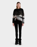 A woman stands facing forward, wearing Rudsak's IZZY - 9525557 Black W winter boots, black leggings, and a black and white alpine crewneck with a mountain and skier design against a plain light gray background.