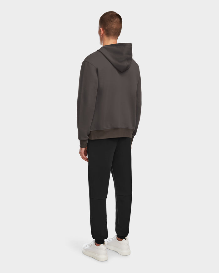 A person faces away from the camera, wearing the Rudsak JACE - 9524010 Grey M unisex zip-up hoodie, black pants, and white sneakers against a plain light background.