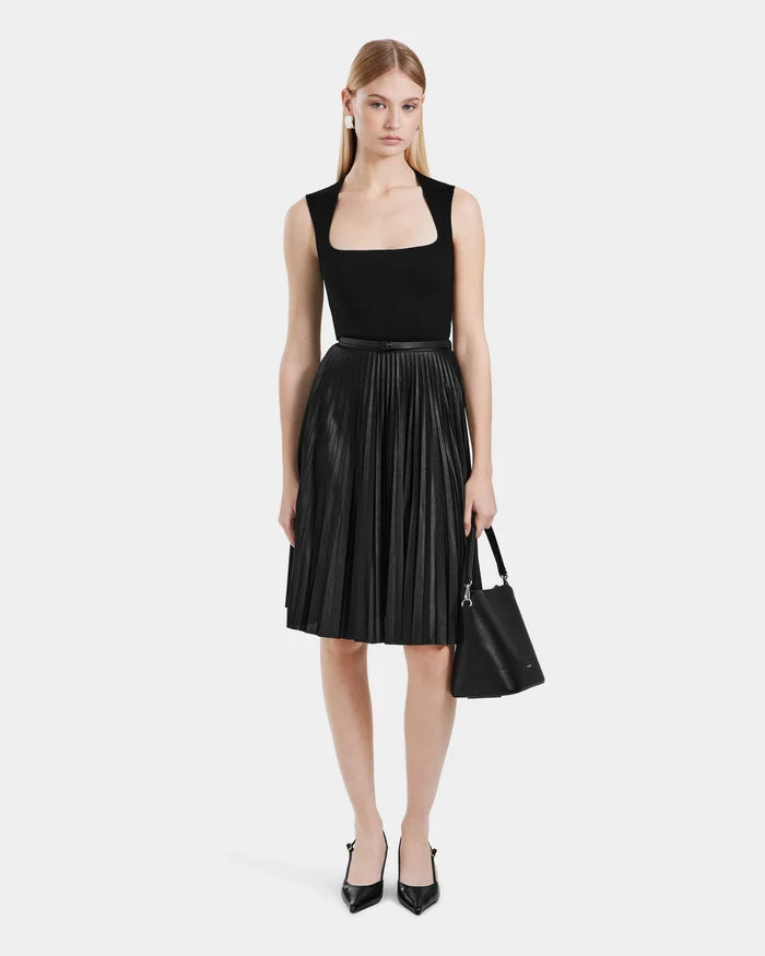 A woman faces forward in a sleeveless, pleated black dress (Rudsak JANE - 8525029), paired with black heels and a black handbag. Her straight hair is worn down.