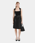 A woman faces forward in a sleeveless, pleated black dress (Rudsak JANE - 8525029), paired with black heels and a black handbag. Her straight hair is worn down.