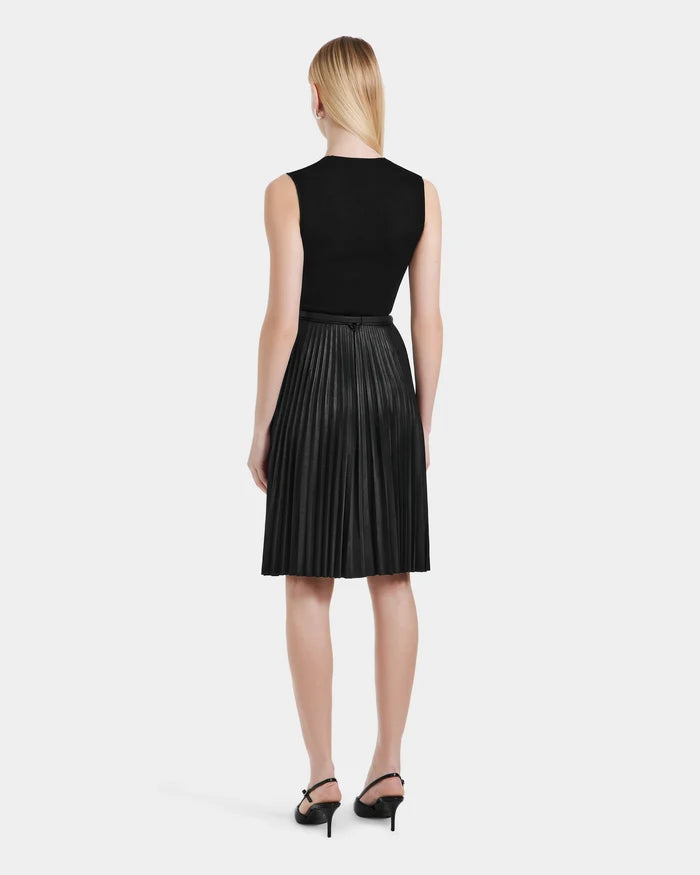 A woman with straight blonde hair, facing away, wears the Rudsak JANE - 8525029 Black pleated midi skirt and sleeveless black top, paired with black heeled sandals against a plain white background.