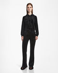 A woman faces forward wearing Rudsak’s JODIE - L523501 Black velour hoodie and matching velvet pull-on pants with an elastic waistband and straight-leg fit, paired with black open-toe slides against a plain white background.