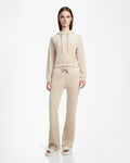 A woman stands facing forward, wearing the Rudsak JODIE - L523501 Cream hooded sweatshirt and sweatpants, paired with slide sandals, against a plain white background.