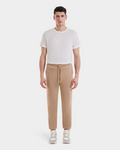 A man stands facing forward against a white background, wearing Rudsak JOSS - 9524009 Almond M premium cotton joggers with a plain white T-shirt and beige sneakers.