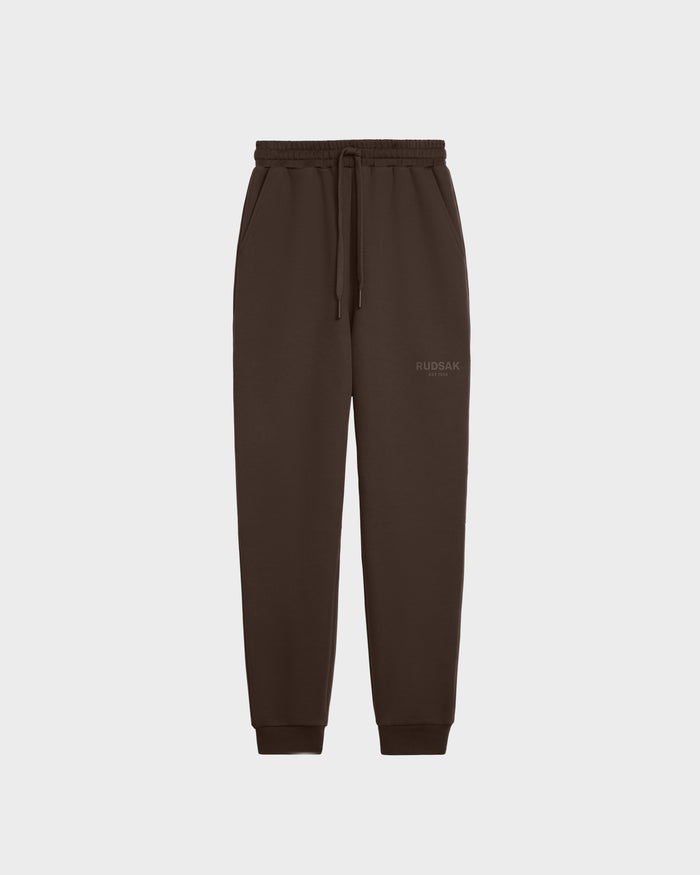 The JOSS - 9524009 Espresso W by Rudsak is a dark brown unisex jogger made of premium cotton with an elastic waistband, drawstring, side pockets, ribbed cuffs, and a subtle Rudsak logo on the left thigh. Displayed on a plain white background.