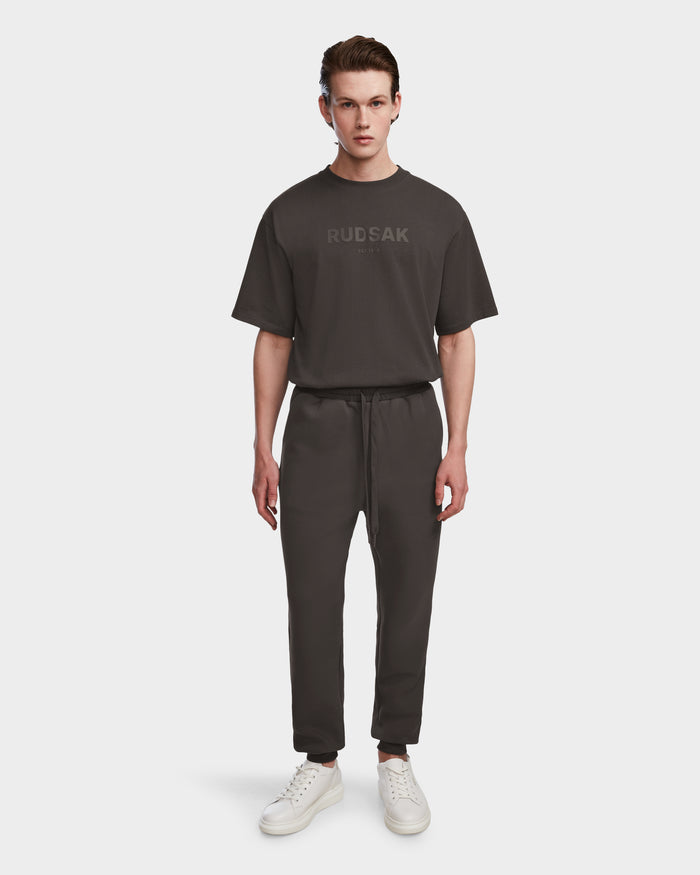 A young man faces forward against a plain white background, wearing the Rudsak JOSS - 9524009 Grey M t-shirt, premium cotton joggers, and white sneakers.