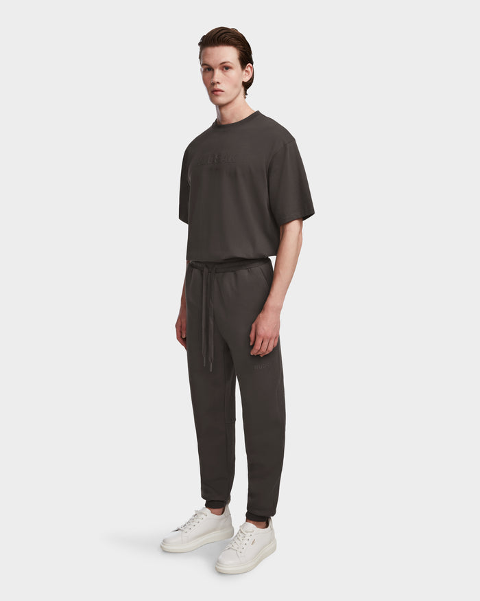 A young man stands against a white background wearing Rudsak’s JOSS - 9524009 Grey M t-shirt and premium joggers with drawstrings, paired with white sneakers.