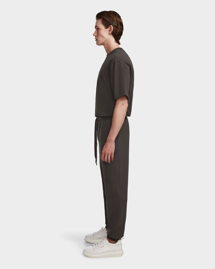 A person in profile against a white background wears the Rudsak JOSS - 9524009 Grey M short-sleeve shirt and premium cotton joggers with a waist tie, paired with white sneakers.