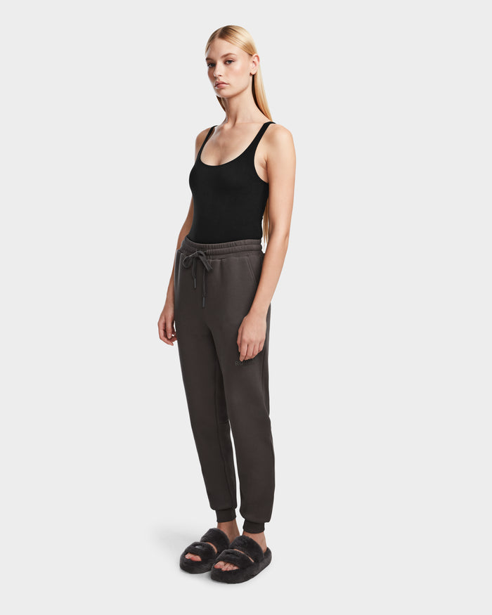 A woman with long blonde hair wears black sandals and a black tank top, paired with Rudsak JOSS - 9524009 Grey W premium cotton joggers in charcoal gray, standing against a plain white background.