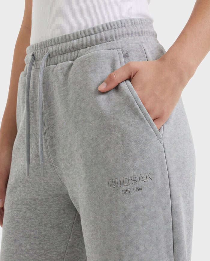 A person wears Rudsak’s JOSS - 9524009 Heather Grey W joggers, made of premium cotton with an elastic drawstring waist and the RUDSAK logo plus EST. 1994 embroidered below the pocket. One hand is in the pocket.