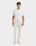 A man faces forward against a plain light background, wearing the Rudsak JOSS - 9524009 Vanilla M premium cotton joggers in cream, a white short-sleeve t-shirt, and beige-white sneakers.