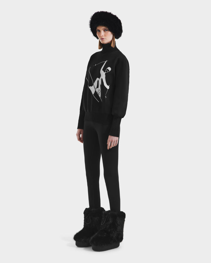 Against a plain white background, a person wears the Rudsak JOYCE - 8525647 Black sweater with an abstract white design, paired with black leggings, furry boots, and a black furry hat for a modern monochromatic look.