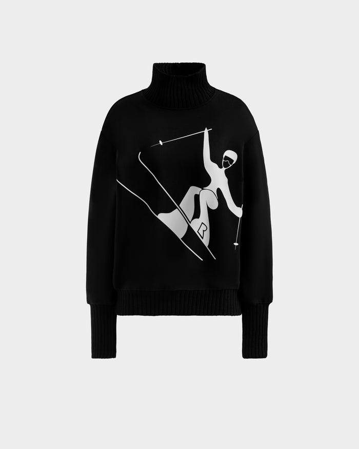 The JOYCE - 8525647 Black by Rudsak is a black turtleneck women’s ski sweater with a white skier graphic, offering retro-inspired après-ski style, shown on a plain light gray background.