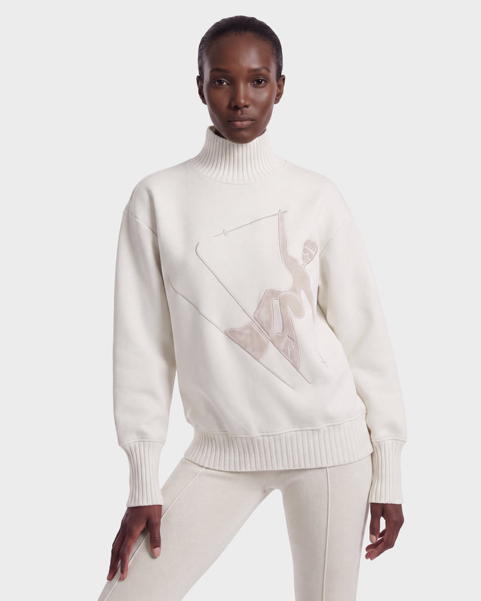 A person wearing the Rudsak JOYCE E - 8526538 Vanilla turtleneck sweatshirt, featuring a minimalist line drawing on the front and paired with matching off-white pants, stands against a plain white background.