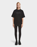 A woman with straight blonde hair wears Rudsaks KARTER - 9524008 Black W, a relaxed-fit oversized unisex premium cotton T-shirt with RUDSAK and MONTREAL on the front, paired with black leggings and shoes against a white background.