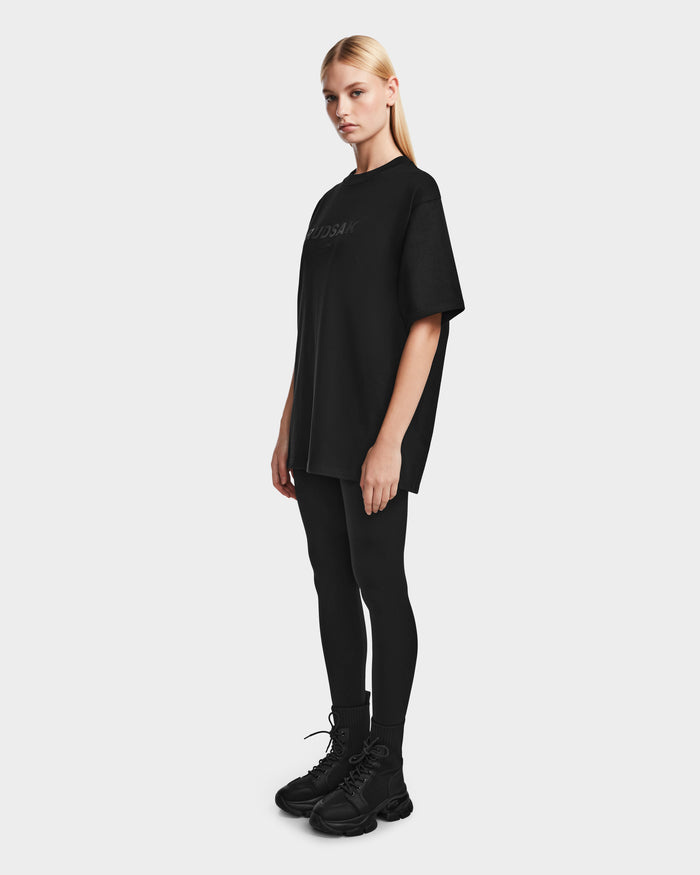 A woman in black wears the Rudsak KARTER - 9524008 Black W, a relaxed fit, oversized unisex T-shirt made from premium cotton for optimal comfort and effortless style.