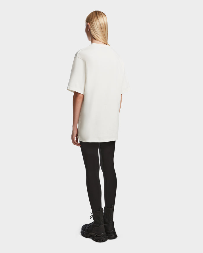 A person with long blond hair faces away, wearing the Rudsak KARTER - 9524008 Iceland W premium cotton T-shirt, black leggings, and black boots against a plain white background.