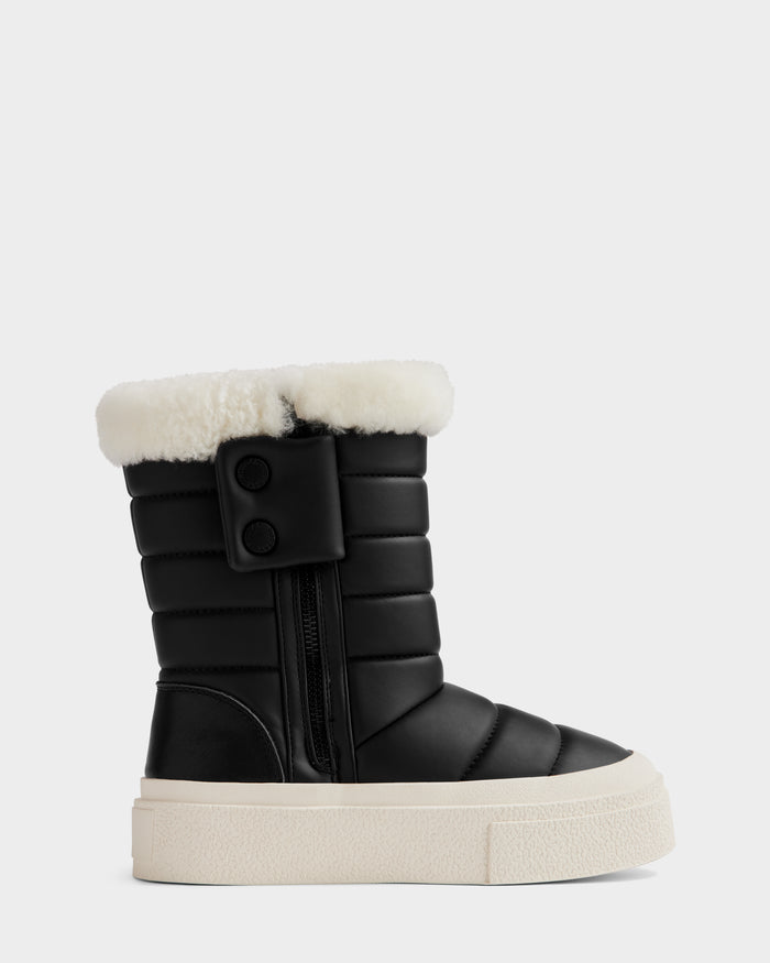 The KATHIE - L225516 Black by Rudsak is a black quilted women's mid boot in vegan leather with a thick white sole, side zipper, two black buttons, and white faux fur trim, shown in side profile on a gray background.