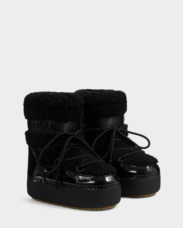 The Rudsak KATHY Y - 1224500 Black boots feature water-repellent shearling uppers, glossy patent leather accents, thick textured soles, black laces, and an insulated look for cozy winter wear.
