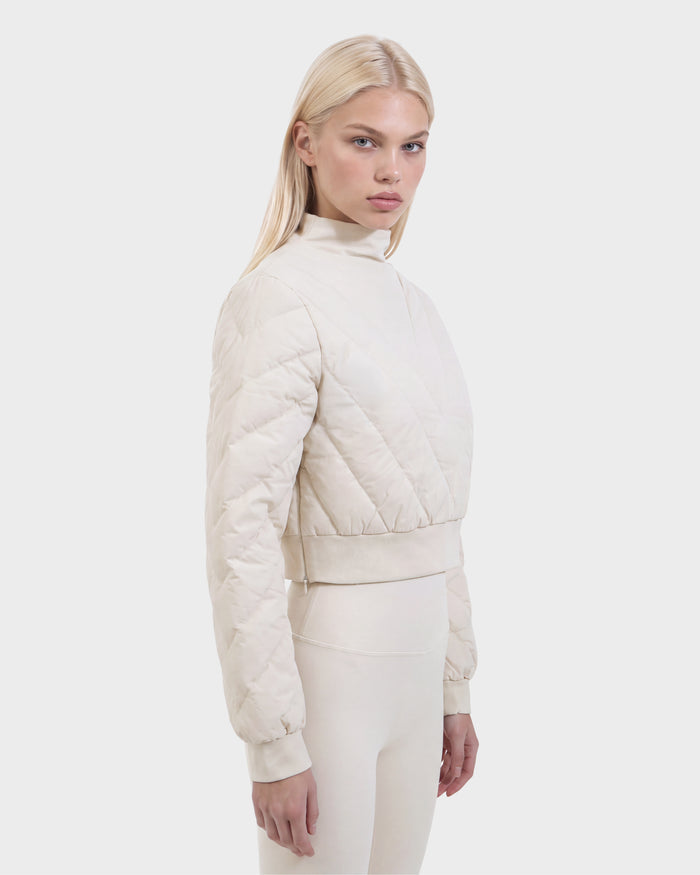 A woman with long blonde hair wears the Rudsak KATYA - 8526531 Vanilla cream quilted jacket with down insulation and matching pants, standing against a plain white background, looking slightly to the side.