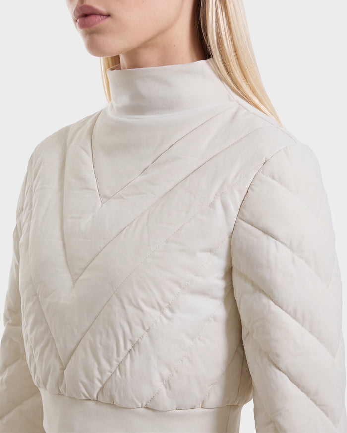 A woman is shown from the shoulders up against a plain white background, wearing the Rudsak KATYA - 8526531 Vanilla jacket—a cream-colored, quilted piece featuring a high collar and chevron stitching inspired by après-ski style.