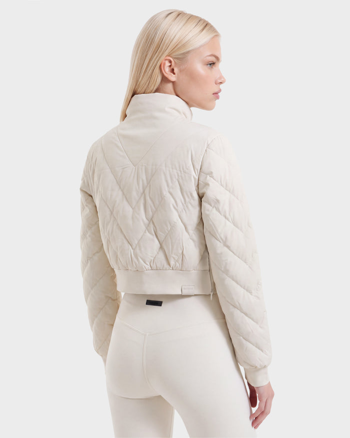 A woman with long blonde hair models the Rudsak KATYA - 8526531 Vanilla cream quilted jacket with down insulation, paired with matching high-waisted leggings, standing with her back to the camera against a plain white background.