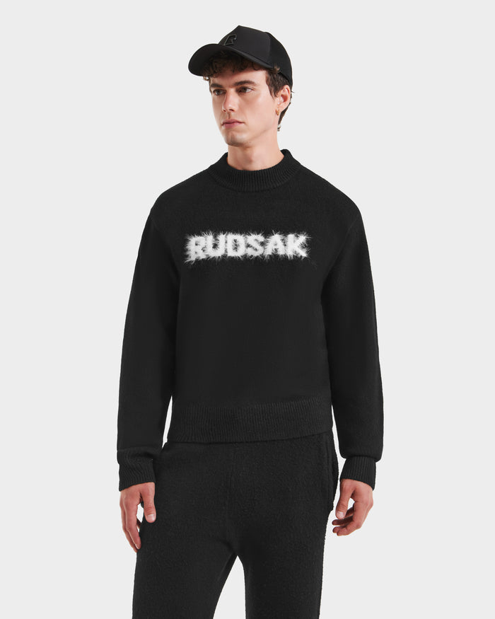A young man wearing the Rudsak KINLEY - 9525555 Black M sweater and matching black pants stands against a plain white background.
