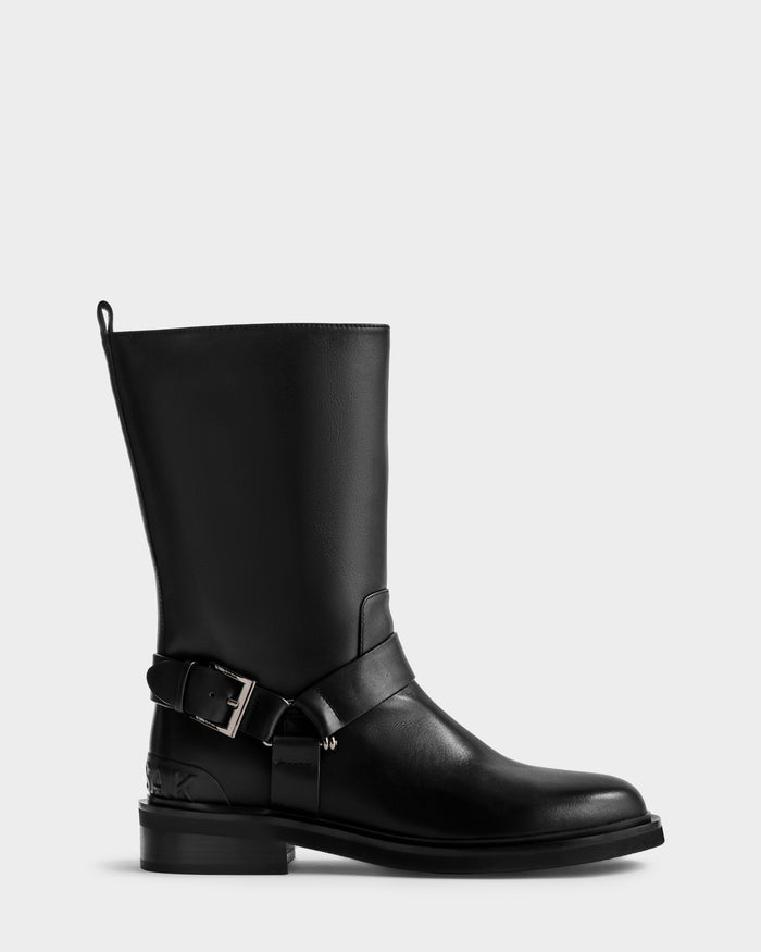 The KIRRA - 8225558 Black by Rudsak is a black leather mid-calf moto boot featuring a low heel, ankle buckle strap, and pull tab detail. Shown on a light gray background, it perfectly embodies Rudsak’s iconic leather boot style.