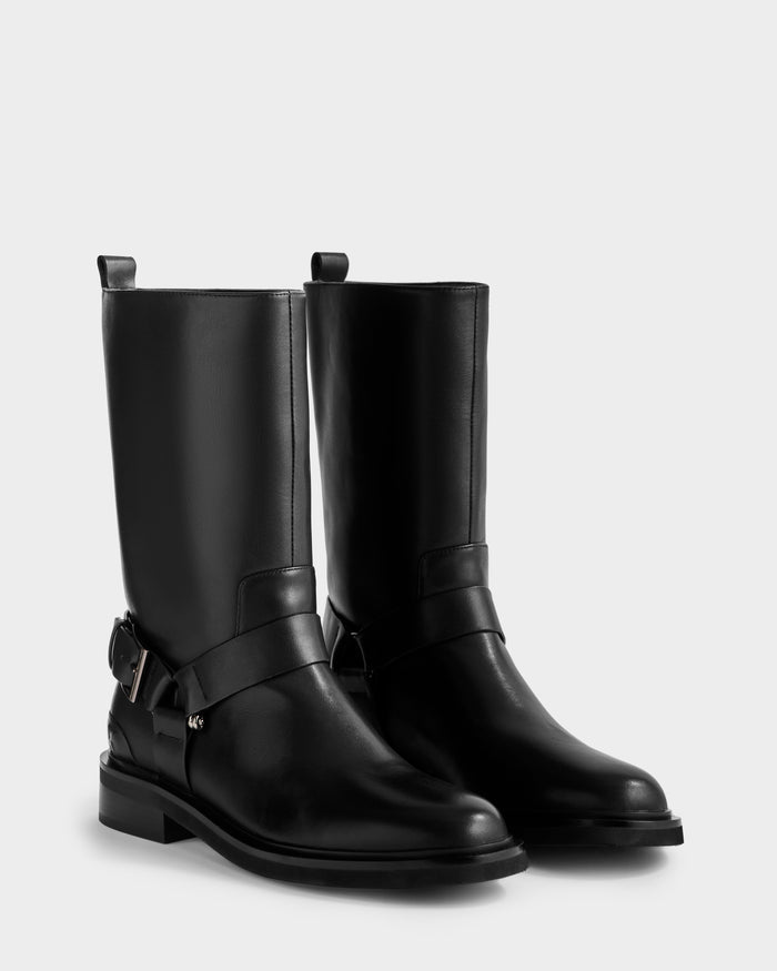 The KIRRA - 8225558 Black by Rudsak are black leather moto boots with low block heel, decorative straps, and silver buckles, shown against a plain light background.