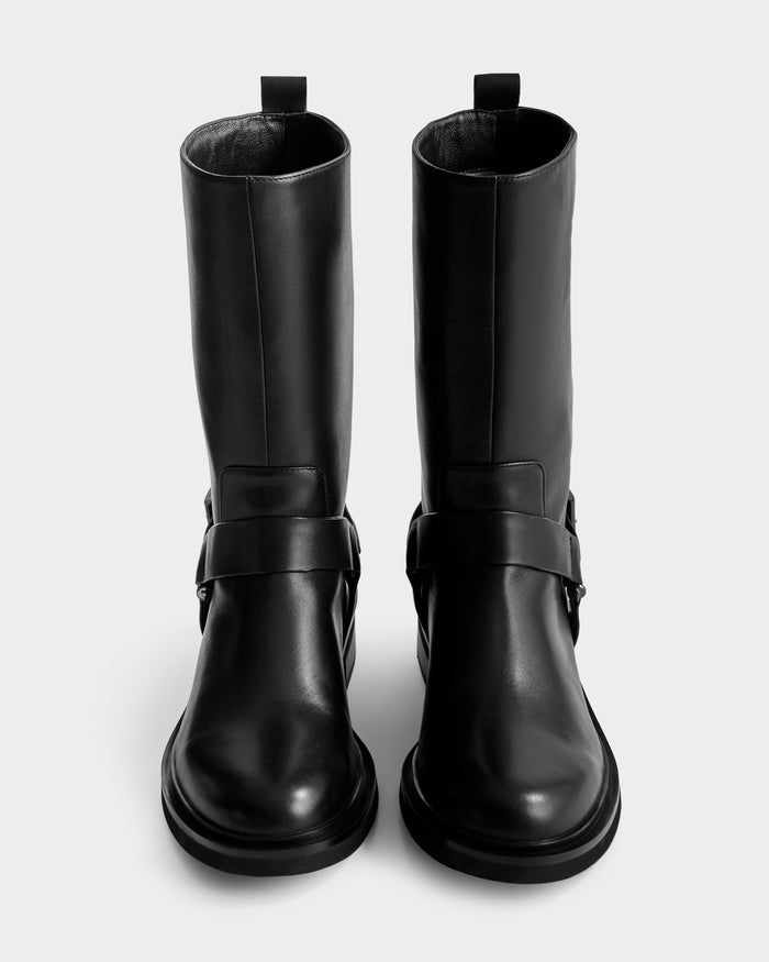 A pair of tall, black Rudsak KIRRA - 8225558 moto boots with straps and a small buckle detail, seen from a top-down front view against a plain, light background.