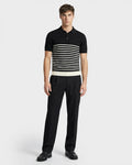 A man faces forward wearing the Rudsak KRIS - 6526005 Black fine-gauge knit polo with bold white chest stripes and black dress pants, set against a plain white background for a sharp, graphic look.