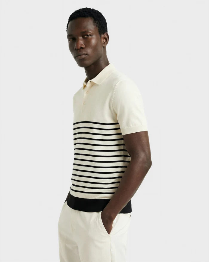 A man wears the KRIS - 6526005 Iceland men’s summer polo by Rudsak, featuring black contrast stripes, paired with cream pants. He stands with hands in pockets against a plain light background, looking at the camera.