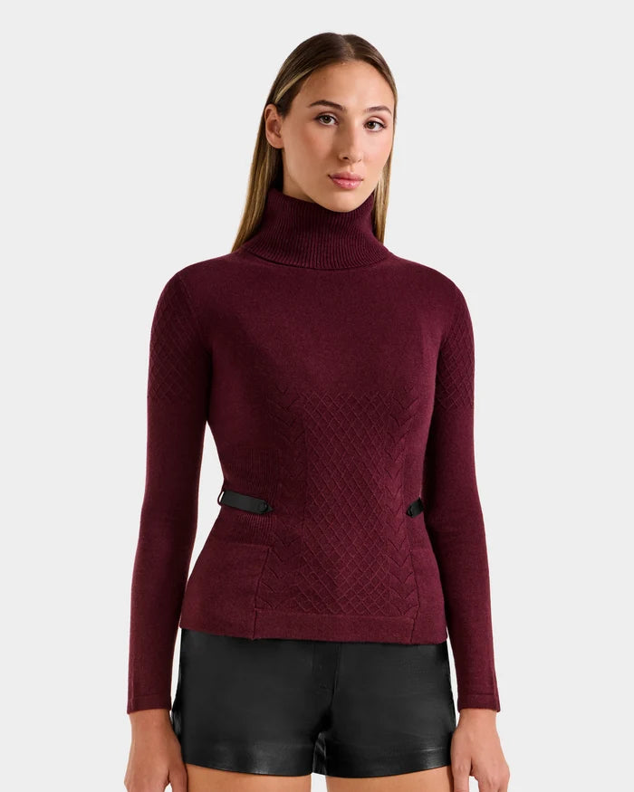 A woman with straight, light brown hair wears the Rudsak LAURA - 8524596 Bordeaux women's knit turtleneck sweater paired with black leather shorts, standing against a plain light gray background.