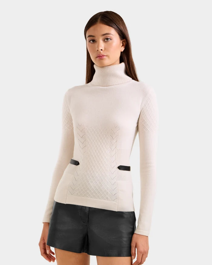 A woman wearing the Rudsak LAURA - 8524596 Vanilla knit turtleneck sweater and black faux leather shorts stands against a plain light background, looking at the camera with a neutral expression.